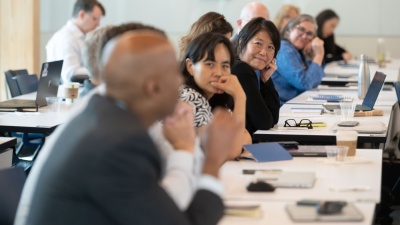 A group of faculty leaders are pictured together for a workshop, seating in a row at a long table. The camera is focused on Julie Kim, who is a member of a past cohort of ACC ALN Fellows.