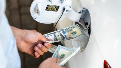 Hand of the man putting money into the opening gas tank of his car. Refueling car with gasoline at gas stations. 
