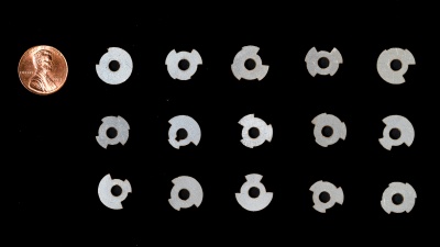 A group of 15 round metal tags of various shapes and a penny to show the tags are smaller.