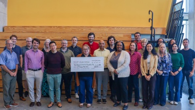 A group photo of more than a dozen people. A woman in the center is holding a large check for Klemis Kitchen, Georgia Tech's on-campus food pantry. 