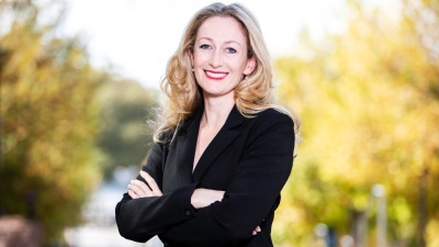 Cassidy Sugimoto standing in a black suit in front of a road lined with trees.