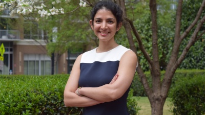 Farzaneh Najafi standing outside smiling with her arms crossed. Green foliage is visible in the background.