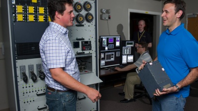 GTRI researchers Duston Cline and Michael Coulter (l-r standing) discuss the AN/AAR-57 integrated support station project, while researcher Nicholas Rodine monitors screen displays for test results. GTRI and the Army Reprogramming Analysis Team (ARAT) have developed and built a new integrated support station (ISS) for the AN/AAR-57 Common Missile Warning System. (Photo: Rob Felt)