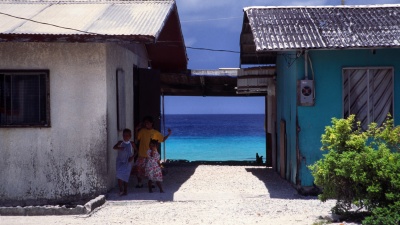 Children are shown with buildings in Majuro, the Marshall Islands, with the sea nearby. The Marshall Islands are facing effects of climate change as sea levels rise. (Credit: Wikimedia Commons)