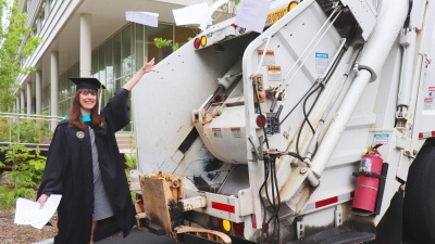 image of Emma Brodzik in master's garb with recycling truck