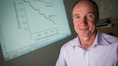 Georgia Tech Professor Gregory Gibson poses with a chart showing death rate differentials between two groups of coronary artery disease patients identified with a new gene expression profile. (Credit: Rob Felt)