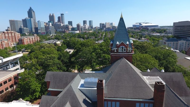 Aerial view of Georgia Tech’s historic campus in Atlanta, with the Tech Tower prominently in the foreground and the Atlanta skyline visible in the background under a clear blue sky.