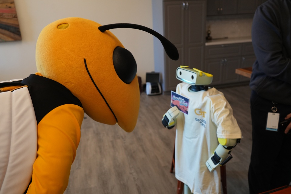 Photo of Buzz the mascot leaning down toward a small humanoid robot wearing a Georgia Tech t-shirt