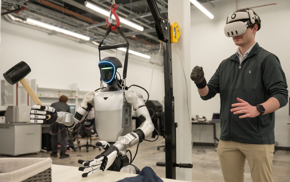 This is an image of someone using VR goggles and a glove to control a humanoid robot holding a rubber mallet.