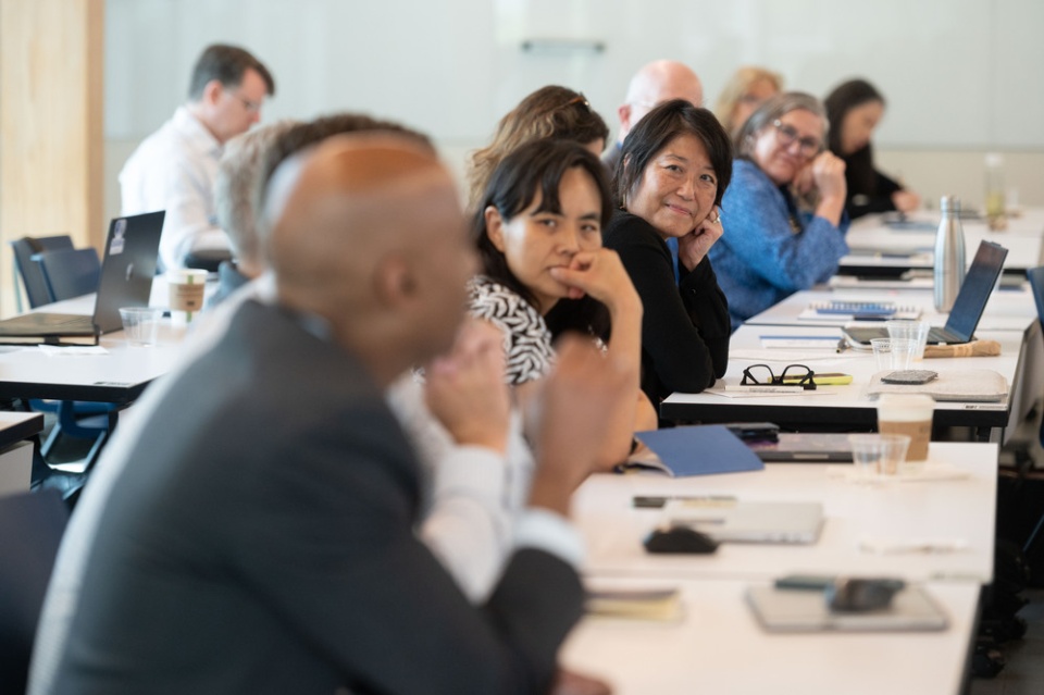 A group of faculty leaders are pictured together for a workshop, seating in a row at a long table. The camera is focused on Julie Kim, who is a member of a past cohort of ACC ALN Fellows.