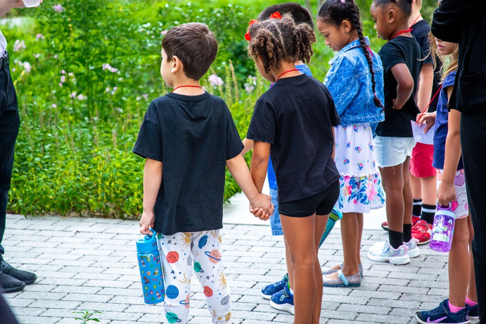 preschool-aged children hold hands and observe as they learn about composting.