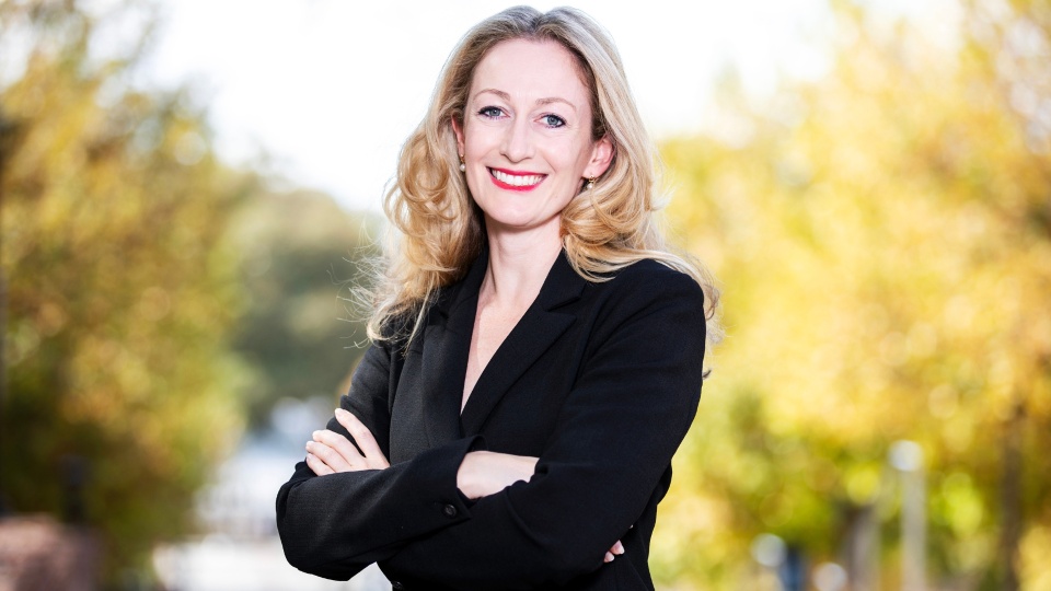 Cassidy Sugimoto standing in a black suit in front of a road lined with trees.