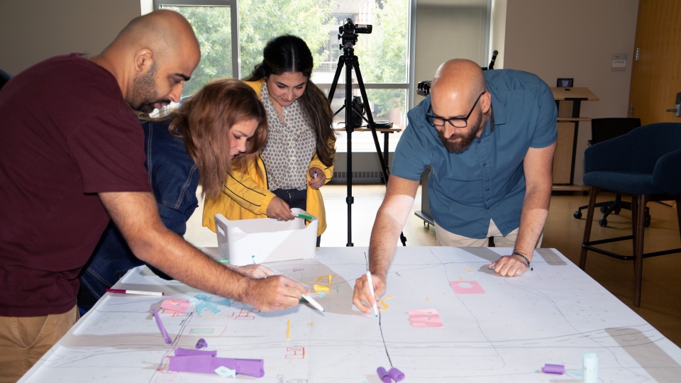 Attendees at the Spatial Scholarship Field School lean over a large table workspace marking up a map.